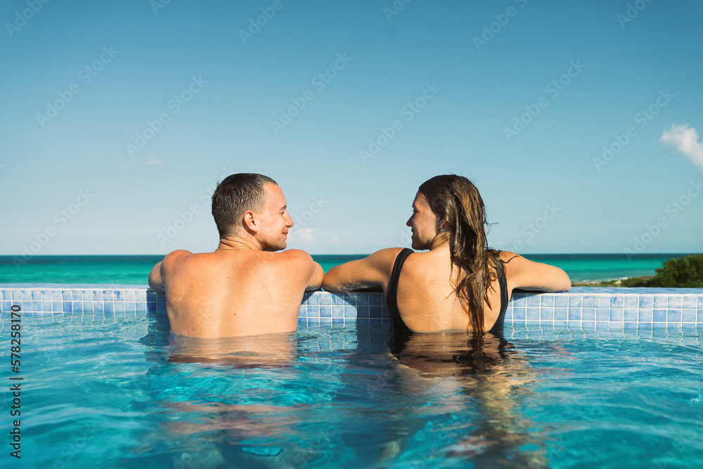 Man looking at girlfriend spending vacation in swimming pool Man looking at girlfriend spending vacation in swimming pool