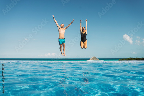 Carefree couple with arms raised jumping in swimming pool photo