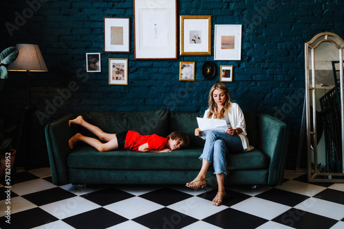 Woman with documents sitting by boy lying on sofa at studio photo