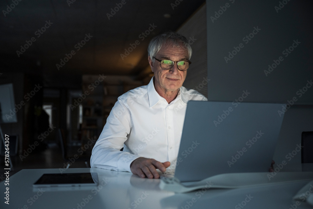 Elderly businessman using laptop sitting at desk in office Elderly businessman using laptop sitting at desk in office