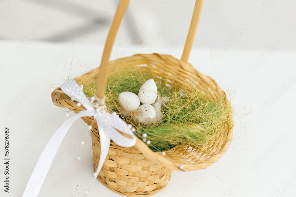 Easter eggs in a basket. Chicken eggs, twigs with green leaves on the hay. Easter holiday concept background. Copy space, white background.