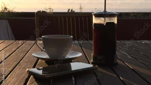 Café recién hecho en cafetera de émbolo con bonita luz de amanecer y móvil y gafas de lectura entran en el plano.
