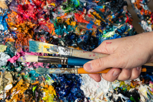 Close-up of the artist's hand with brushes on a background of multicoloured paints