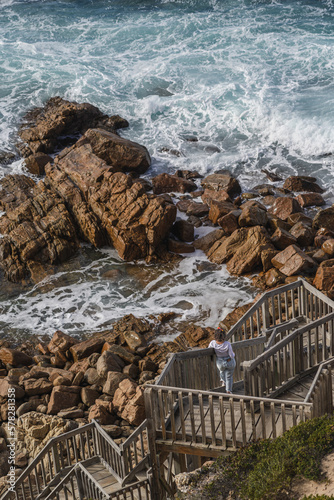Women with short hair and white tshirt stand up in wood stair looking to the rocks and sea in a beatiful coast landscape