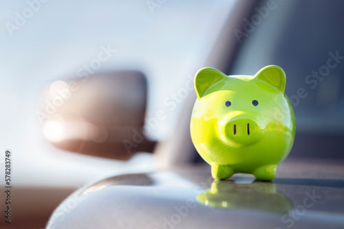 Slika na platnu Green piggy bank money box on top of car hood, new vehicle purchase, insurance o