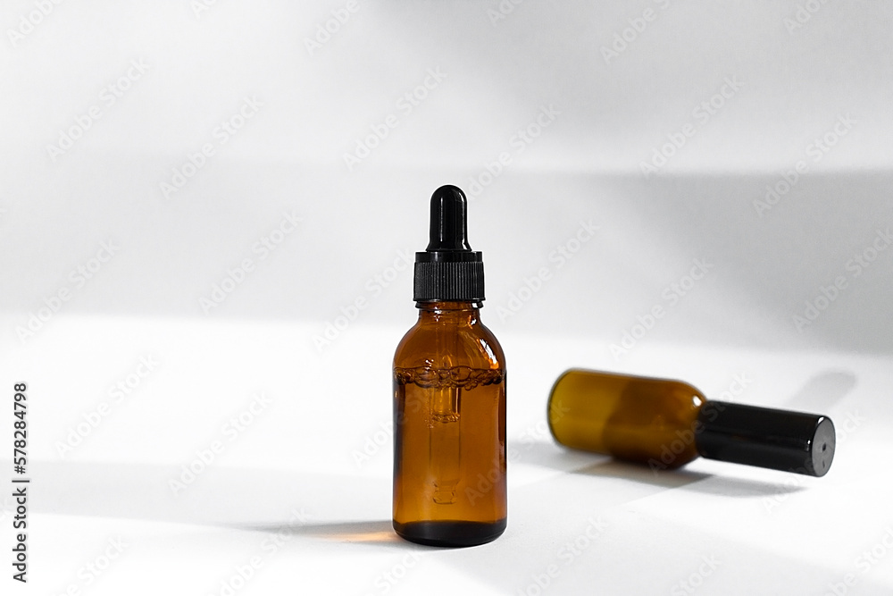 Glass cosmetic bottles with a dropper on a white background with hard shadows. The concept of natural cosmetics, natural essential oil Glass cosmetic bottles with a dropper on a white background with hard shadows. The concept of natural cosmetics, natural essential oil
