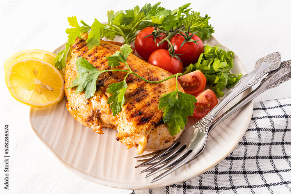 large textured ceramic plate with grilled chicken fillet with fresh vegetables. lemon wedges to improve the taste. white background.