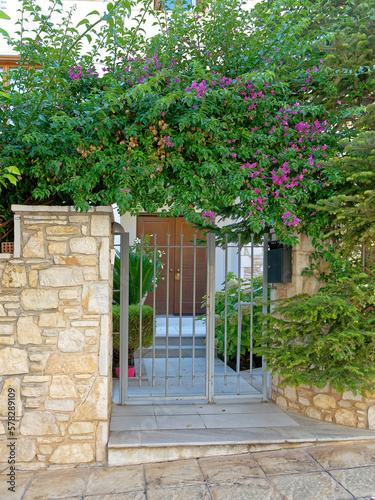A vintage house main entrance with stone fence and green foliage by the sidewalk.