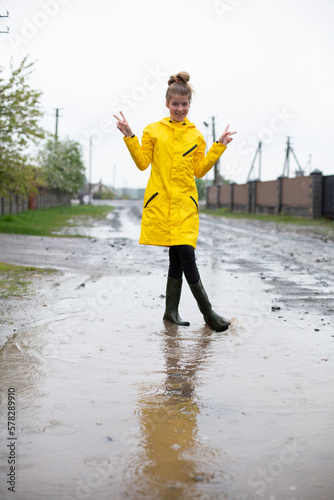  girl in a yellow raincoat walks through puddles in the rain. jump in puddles. to rejoice in the spring rain. rainy weather and beautiful girl