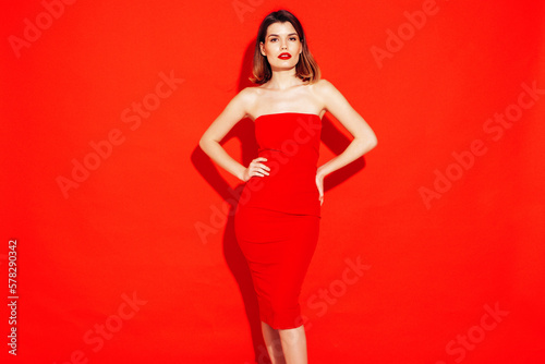 Portrait of young beautiful smiling female in trendy summer red evening dress. Sexy carefree brunette woman posing in studio, isolated. Positive model with evening makeup. Cheerful and happy