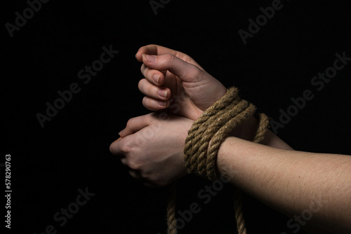 Women's hands tied with a rope on a black background. photo