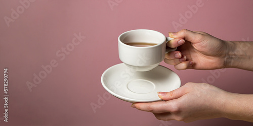Female hands holding a cup of tea and a saucer on a pink background