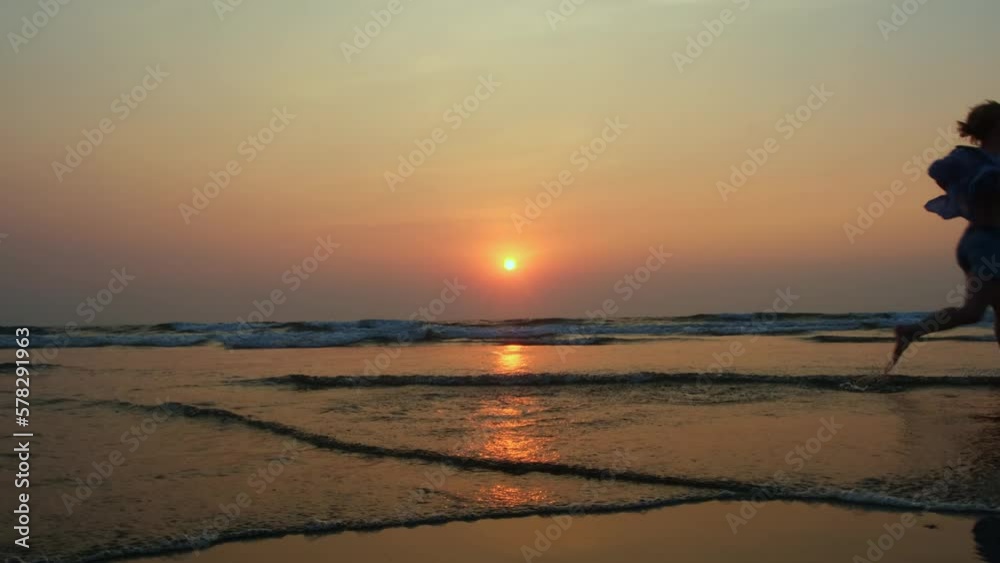 Silhouette of a slender woman running on the beach against the setting sun background. Female silhouette on the seashore at sunset. Silhouette of a slender woman running on the beach against the setting sun background. Female silhouette on the seashore at sunset.