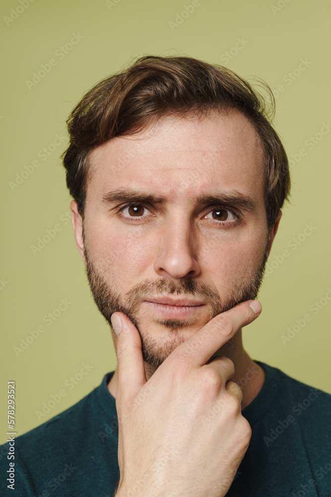 Pensive man touching his chin and looking at camera isolated over green wall