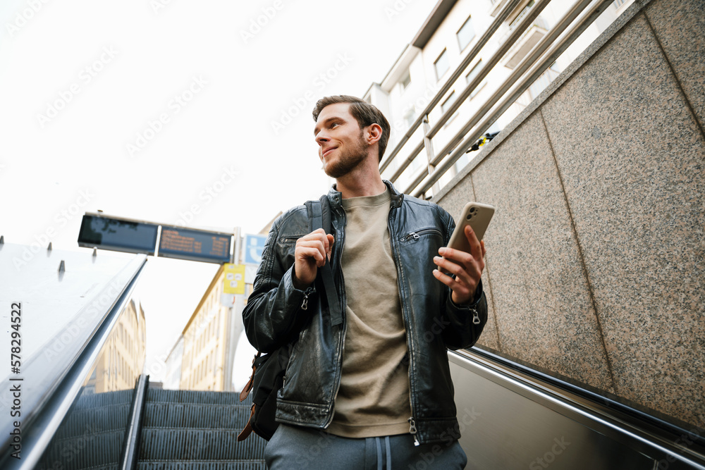 Young man using mobile phone while going down escalator outdoors Young man using mobile phone while going down escalator outdoors