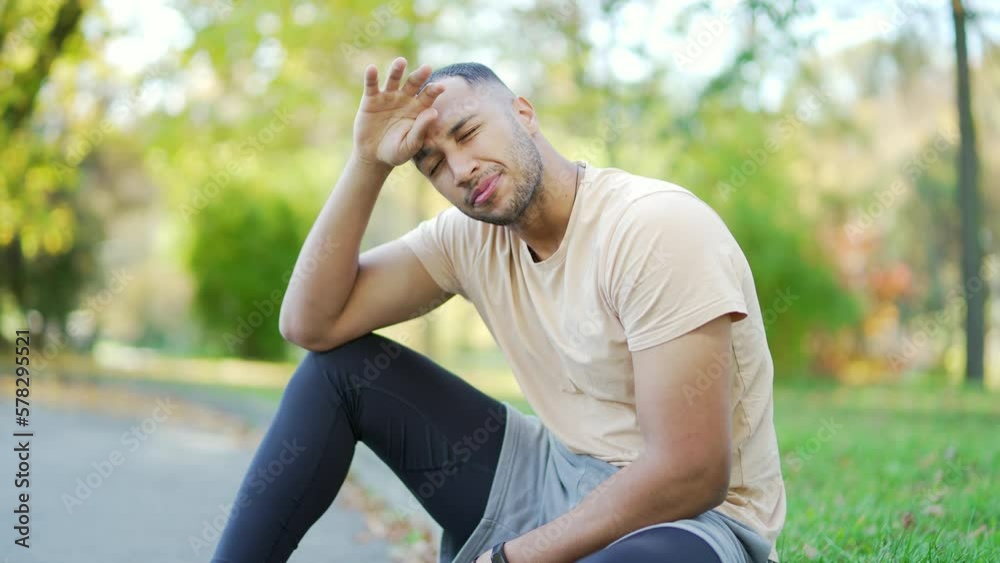 Close up of a young runner in a t-shirt overtired after a hard run sitting in an urban city park. Male taking a rest as he tries to catch his breath and recover from the intense physical exertion