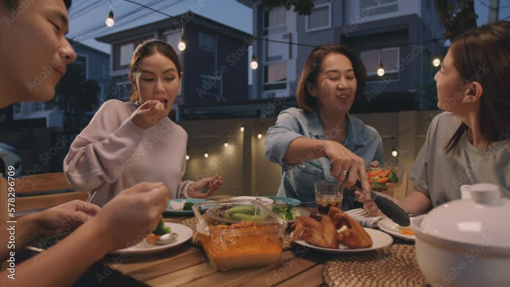 Mom enjoy thai meal cooking for family day home dining at dine table cozy patio. Mum passing serving food to group four asia people young adult man woman friend fun joy relax warm night picnic eating.