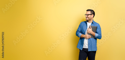 Man holding laptop looking away smiling against yellow background