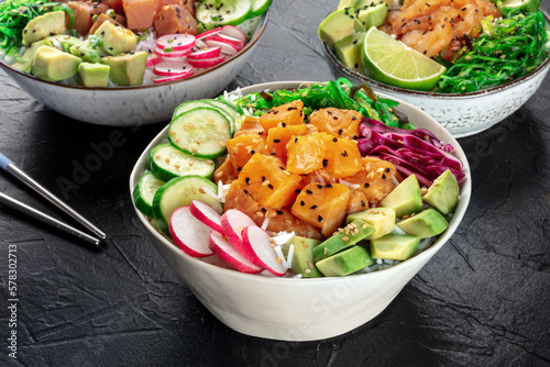 Poke bowl variety. Healthy Hawaiian dish with salmon, tuna, and shrimps, on a black slate background with chopsticks photo