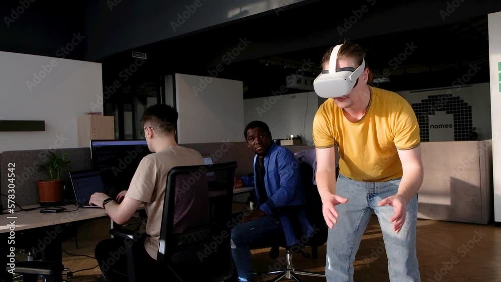 IT Development Team Working on VR Project. Man wearing VR headset, playing and touching something in the virtual world. Diverse men programmers using VR technologies and computer to create video game. IT Development Team Working on VR Project. Man wearing VR headset, playing and touching something in the virtual world. Diverse men programmers using VR technologies and computer to create video game.