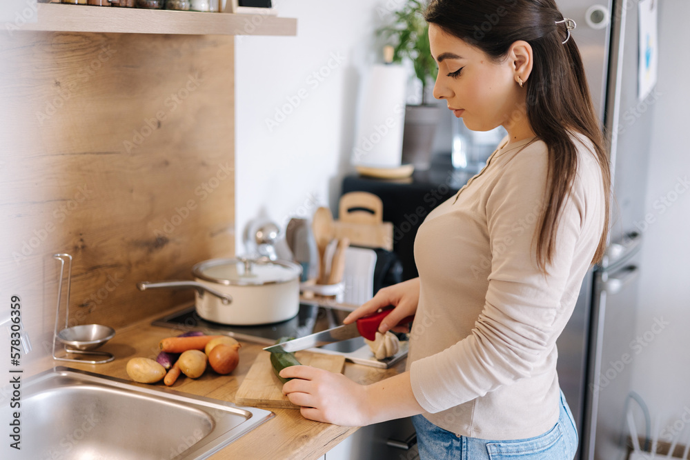 Beautiful young female cutting vegetables on kitchen at home. Home food concept Beautiful young female cutting vegetables on kitchen at home. Home food concept