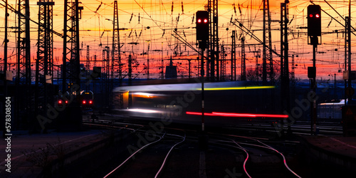 Trains in motion at Dortmund station in warm evening light. Curved main line railway tracks glistening in the sun. Longtime exposure panorama of public transport in Ruhr Basin metropole Germany.