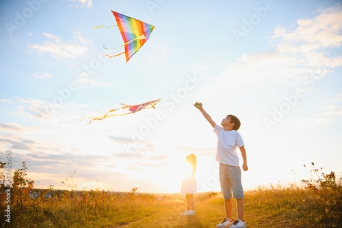 Brother and sister playing with kite and plane at the field on the sunset.