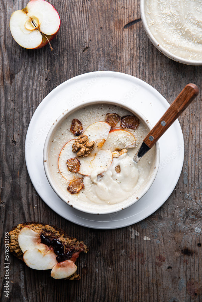 Two bowls of homemade Jerusalem artichoke and apple cream soup and open sandwich with homemade pate with fresh apple and cherry jam on wooden table. Two bowls of homemade Jerusalem artichoke and apple cream soup and open sandwich with homemade pate with fresh apple and cherry jam on wooden table.
