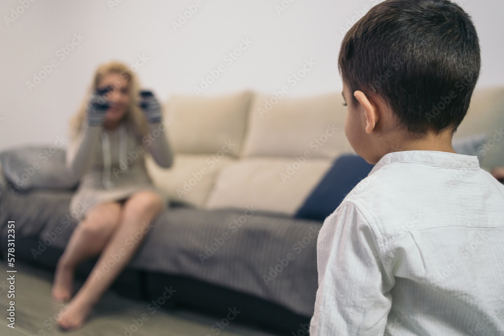 Little autistic boy paying attention to his middle-aged mother who tries to play with him with socks in her hands.