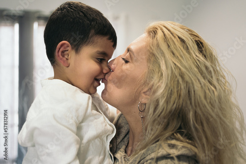 Middle-aged blonde woman face to face with her young autistic son kissing each other on the mouth.