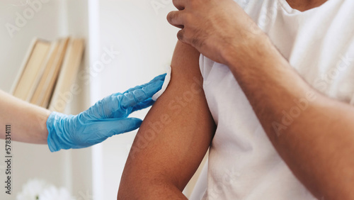 Flu shot. Vaccine inoculation. Virus prevention. Closeup of unrecognizable doctor hand in glove giving injection jab dose to male patient arm shoulder. photo
