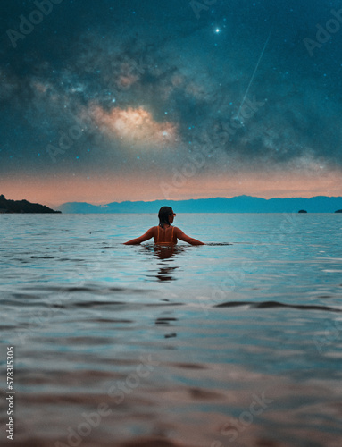 back view beautiful young woman submerged in water up to her torso relaxed with open arms and milky way in the background  © oscargutzo