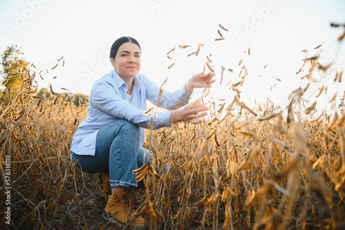Young farmer woman standing in soy field in summer time, holding tablet and monitoring crop growth