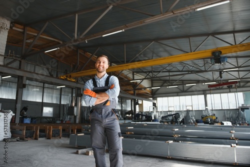 Portrait of factory worker in protective uniform and hardhat standing by industrial machine at production line. People working in industry