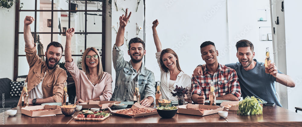 Fototapeta premium Group of happy young people having dinner with pizza indoors together