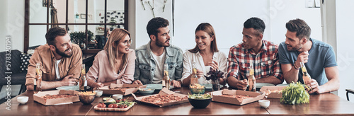 Group of cheerful young people having dinner with pizza indoors together