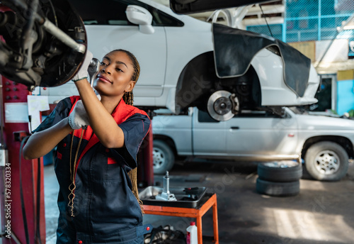 Engineer team checking under car condition on lifter in garage.Young auto mechanic in uniform is looking at camera and smiling examining car...