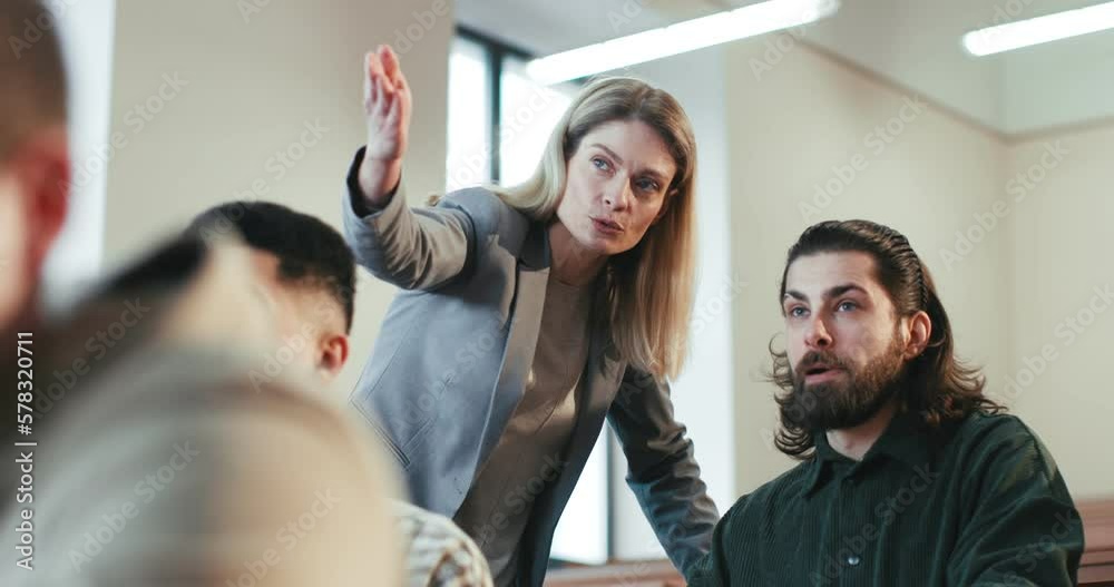 Close up of Caucasian female teacher helping to guy student and explaining him something while pointing at the blackboard. Students at University having exam. Professor at class. Communication. Close up of Caucasian female teacher helping to guy student and explaining him something while pointing at the blackboard. Students at University having exam. Professor at class. Communication.