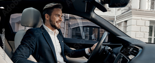 Handsome young man in formal wear smiling while driving a car © gstockstudio