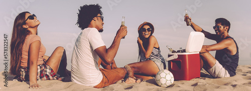 Group of cheerful young people enjoying cold beer while spending time on the beach together