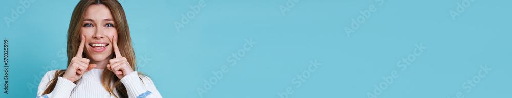 Beautiful young woman looking at camera and smiling while standing against blue background Beautiful young woman looking at camera and smiling while standing against blue background