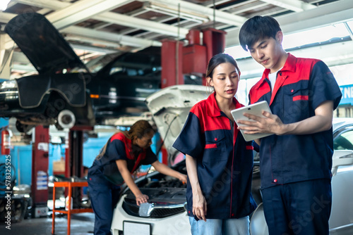 Asian automotive engineer people wear helmet work in mechanics garage.young auto mechanic in uniform is looking at camera and smiling examining car.