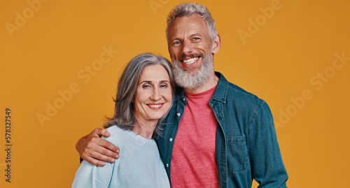 Billede på lærred Beautiful senior couple embracing and smiling while standing against colored bac