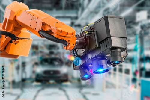 Industrial 3D laser scanner on robotic arm on background of car manufacturing factory. Automated robot arm assembly line manufacturing. Development and production of automotive technologies.