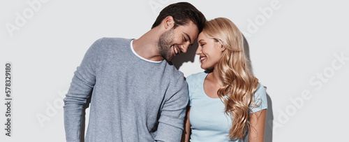 Картината върху платно Young loving couple smiling while standing face to face against grey background