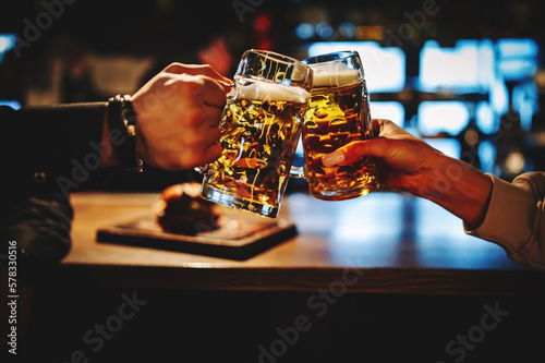 man and woman hands toasting with glasses of light beer at the pub or bar