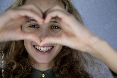 A cute teenage girl makes a heart shape with her hands and fingers and smiles joyfully. Good mood and expression of love