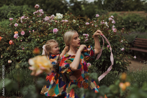 Young mother walking with her little daughter in the rose garden. Portrait mom with child together on nature. Mum, little daughter outdoors. Happy Mothers Day.