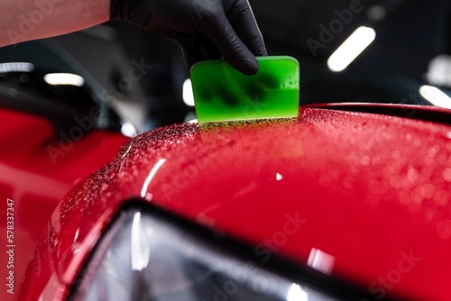 Obraz na płótnie Application of a colorless protective film at a car detailing studio or car wash. Beautiful red car paint. w salonie