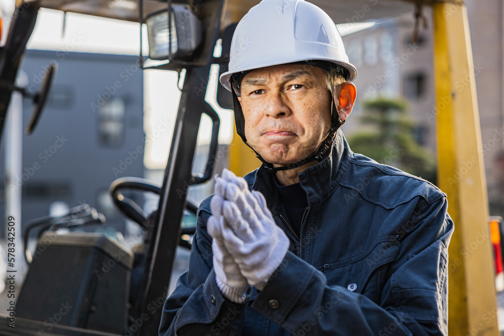Middle-aged Asian male worker with forklift on factory grounds. Middle-aged Asian male worker with forklift on factory grounds.